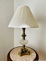 Full view of the vintage brass and crystal base table lamp showing the cream pleated fabric shade, the crystal centerpiece on the base, and detailed brass decorative elements.