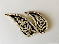 Top view of vintage black and gold enamel brooch with clear rhinestones and an intricate floral and heart pattern.