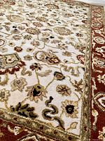 Close-up showing detailed traditional floral and paisley motifs in muted colors on cream background with red border.