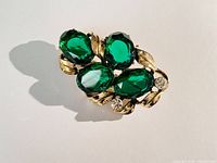 Top angle photo of the vintage large emerald green rhinestone brooch showing four green rhinestones and gold-tone decorative leaves.