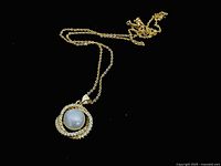 Full view of vintage necklace with gold chain and large pearl pendant on black background