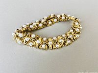 Full view of the gold-tone bracelet shows two rows of faux pearls and rhinestone embellishments in crescent moon-shaped segments with a clasp.