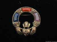 Front view of brooch showing colorful enamel sections in blue, red, and purple with hands holding a crowned heart.