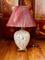 Full view of the vintage table lamp showing the marbleized glass base, brass stand, and pleated plum lampshade on a wooden floor with decorative screen background.