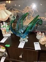 Photo showing the full side view of a large blue and green glass bird sculpture on a wooden cabinet with other vintage items nearby.