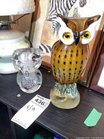 Two Murano glass owl figurines shown on a shelf, larger amber colored with spots and smaller clear textured glass owl