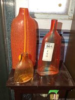 Three art glass vases in amber and red/orange tones on a wooden table, showing size difference and design details