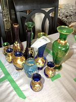 Full view of nine assorted coloured glass vases showing various colors and gold decorations on a table.