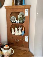 Full view of wooden corner cabinet mounted in corner with some decorative items in display