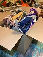 Box filled with multiple porcelain dolls lying in various stacked positions, some partially visible, showing detailed clothing and delicate features.