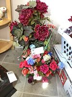 Two different artificial floral arrangements visible, one tall with dark red flowers and grapes, the other a colorful mixed flower basket.