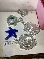 Lot with two larger clear glass turtles, glass turtle candle holder with a tealight candle, clear glass snail, and blue glass starfish on a white surface.