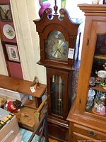 Photo of the full grandfather clock showing the height, wooden case and bonnet top design along with visible weights inside the glass door.