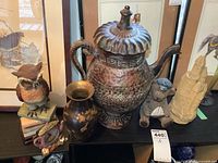 Photo showing the large ornate metal pitcher with lid, brass vase, resin bear, resin castle, and small clock on a dark surface.