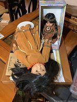 Photo of two indigenous dolls, one laying down with long black hair and bead necklace, other in box with beaded outfit