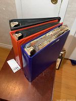 Three closed binders (blue, orange, black) standing on side showing spines and thickness