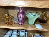 Shelves displaying various Murano and art glass pieces including amber glass dishes, a purple vase, and a green swirled Murano dish