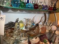 Top view of glass paperweights including colored spheres and abstract shapes on upper glass shelf