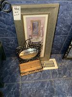 Framed print of bathroom scene on tiled floor with wicker baskets and metal framed mirror in front