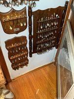 Three different wooden spoon racks mounted on a wall, each filled with an assortment of collectible souvenir spoons
