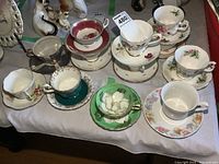 Overview of all 12 teacups and saucers arranged on table, showing variety in style and color