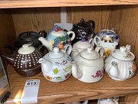 Full grouping of 11 teapots arranged on wood shelf showing various patterns and styles