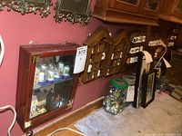 Five small wooden display racks and one small wall-mounted wood-and-glass display case mounted on a wall with various decorative thimbles inside. Some miniature houses and miscellaneous pieces inside the glass case.