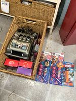Basket containing a vintage slot machine toy labeled 'Buckaroo Bank', other items including two Pop Ups! lollipop packs and PEZ dispenser outside the basket with the basket also containing miniature tea sets in boxes and other items.