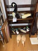 Photo showing the wooden Canada goose duck on a shelf, two ceramic painted ducks below, and two unpainted wooden loons on floor in front.
