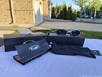 Three-quarter view of sunglasses resting on opened Oakley box with soft pouch and cleaning cloth in front