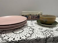 Overall lot view showing pink plates stack, bread plate, bowl and Swiss tin