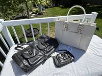 White leather tote, black travel bag, small matching purse on table