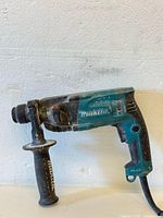 Side view of a used Makita corded drill showing the handle, trigger, and body with visible dirt and wear.