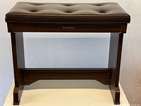 Front view of the wooden piano chair showing padded tufted seat and sturdy frame with Technics logo on front beam.