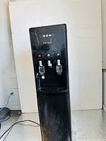 Full front view of the black Primo water dispenser with three spouts and control lights on front panel.