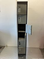 Front view of tall metal storage cabinet with six individual locker doors in gray color, one door open showing inside.