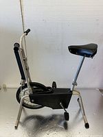 Side view of vintage CCM exercise bike showing seat, pedals, chain cover, and white frame.