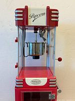 Front view showing 'Popcorn' branding on top and Nostalgia Electrics label on kettle housing, showing the kettle and crank handle.