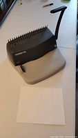 Front view of the GBC Docubind P100 with binding comb pins and handle lever on a white table with aligned paper sheet.