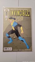 Front cover of Invincible #1 comic book showing main character in blue, black, and yellow superhero suit against cracked gray background.