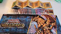 Photo showing the Yu-Gi-Oh cards laid out in front of the game mat and card holder, with the game mat displaying 'Battle Pack 2: War of the Giants' artwork and zones.