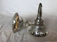 Two silver plated wine funnels lying on their sides, showing overall shape and design.
