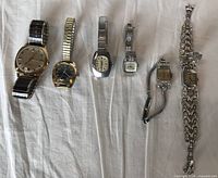 Overview of all six vintage wristwatches laid out on fabric showing variety of sizes, shapes, and band styles.