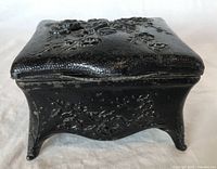 Front angled view showing textured black surface with raised chrysanthemum floral design and curved legs.