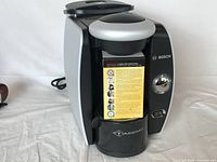 Front view of Bosch Tassimo coffee maker showing the power button, control dial, and Tassimo logo on the coffee dispensing area.