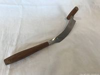 Cheese cutter shown from an angle highlighting the wooden handle and the curved stainless steel blade with a wooden knob on the opposite end of the handle.