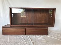 Front view of upper glass door cabinet stacked on two drawer cabinet, showing overall lot setup with teak wood and glass doors.