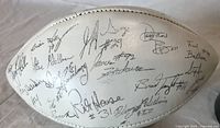 Close-up view of white football with multiple player autographs on the surface in black ink.