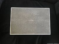 Top view of closed rectangular jewellery box with black and white shagreen pattern and white frame.