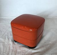 Two-tier Japanese lacquer style box, orange with black interior and feet, closed view showing rounded edges and glossy finish.